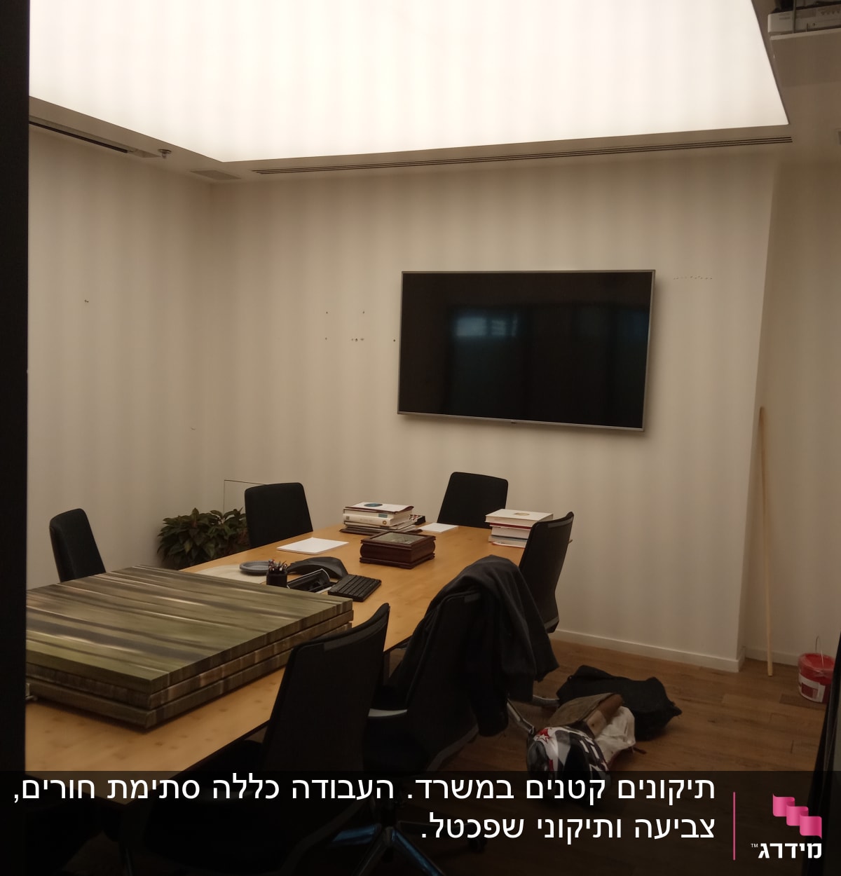 חדר ישיבות עם שולחן, כיסאות ומסך טלוויזיה על הקיר.